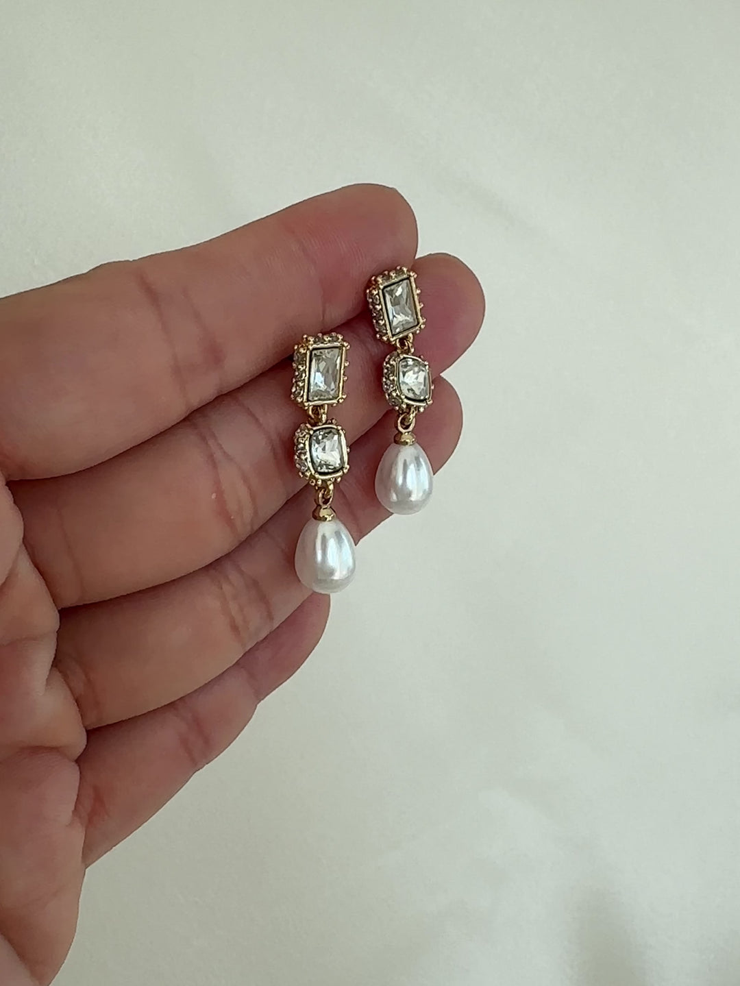 Pair of gold earrings with clear gemstones and a pearl drop